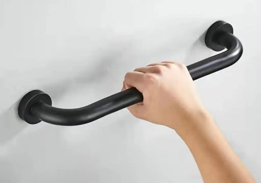 Hand gripping a matt black bent tube grab rail mounted on a wall